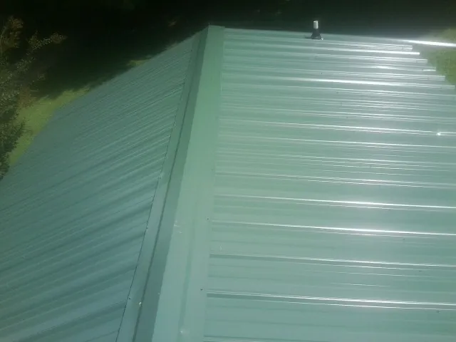 New green metal panels meeting at the ridge of a roof — Flat Roof Repair work by our crew in Central City