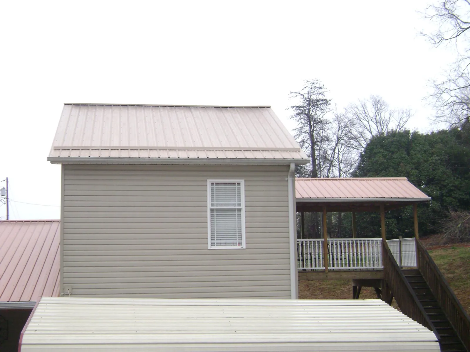 Tan metal roofs on a two story addition and attached porch, from a Roof Replacement job in Central City